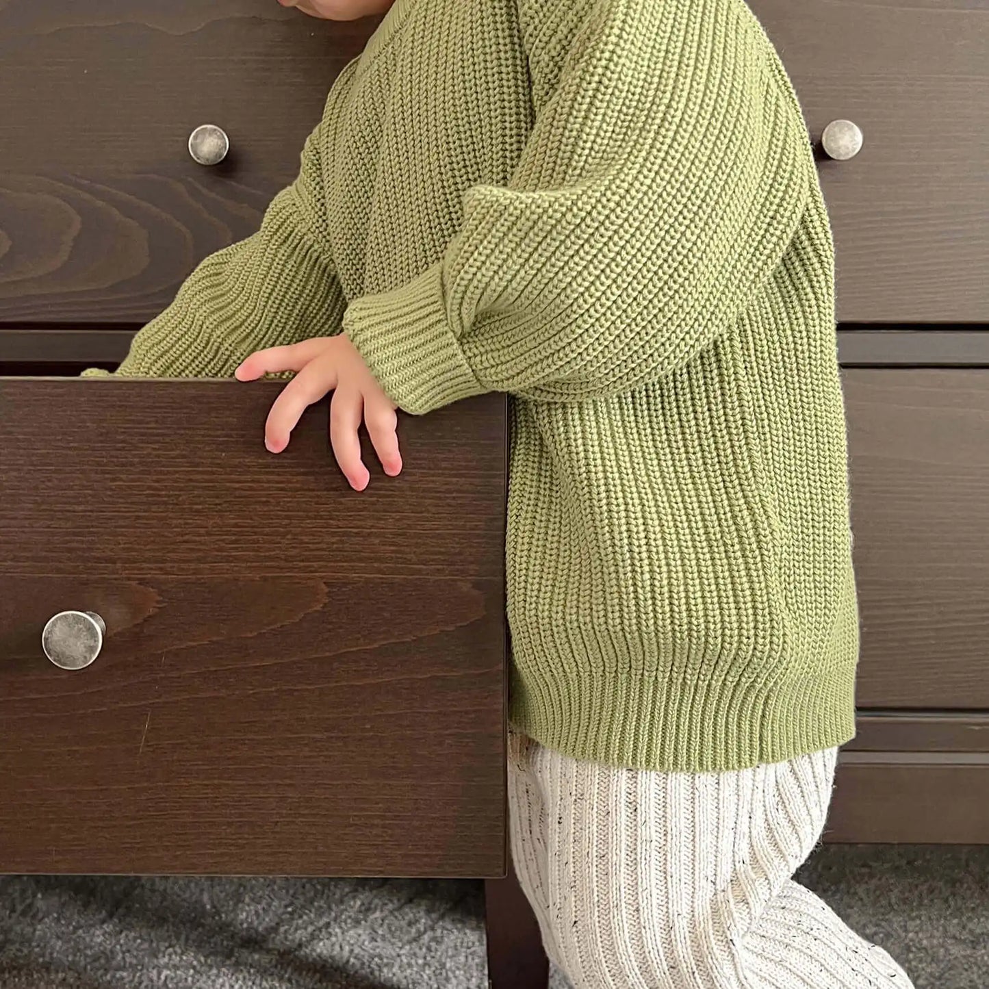 toddler opening a drawer, wearing 100% organic cotton chunky crew knit jumper in moss and chunky leggings in frosty speckle, enjoying a moment of curiosity and comfort
