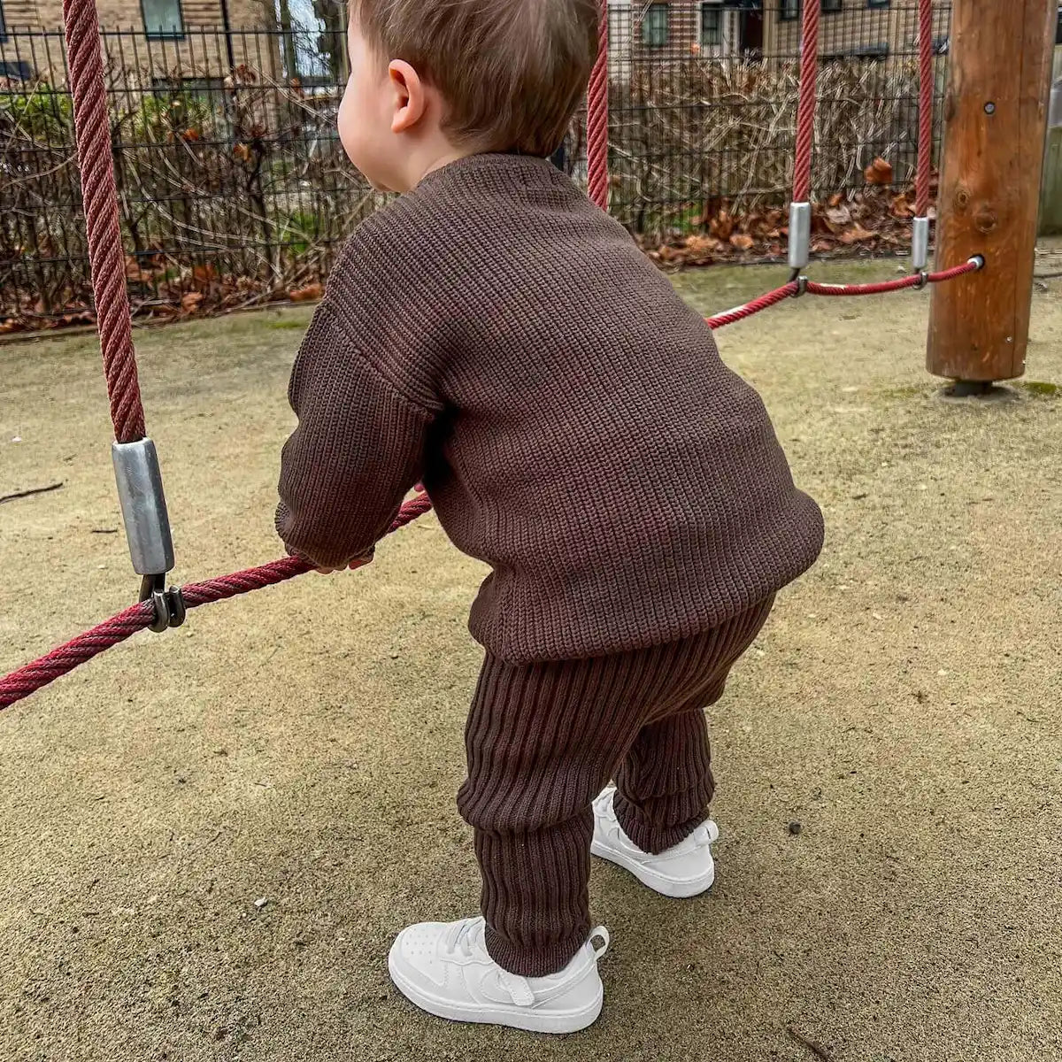 toddler playing at the playground, wearing 100% organic cotton chunky crew knit jumper and chunky knit leggings in cocoa, stylish and cozy for outdoor fun
