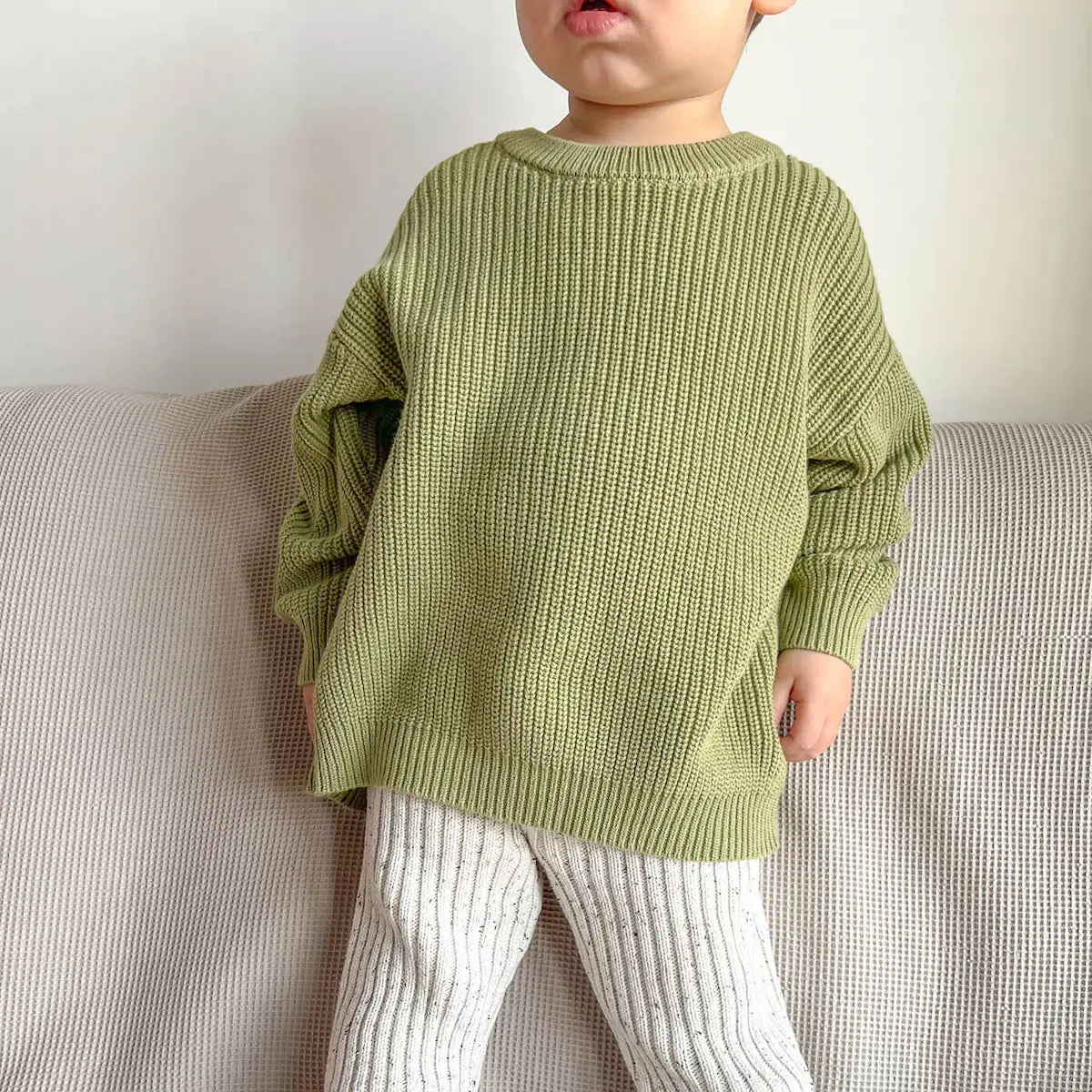 toddler lounging around, wearing a mix and match outfit including chunky crew knit jumper in moss and chunky leggings in frosty speckle, for a playful and cozy look
