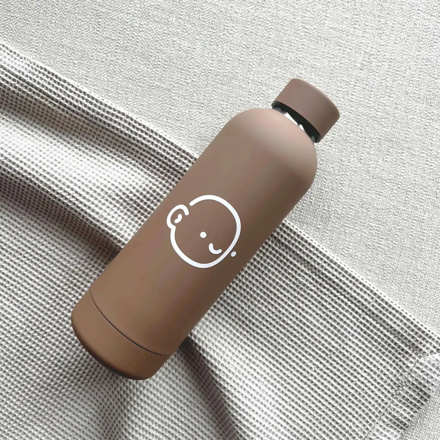 beige tottles stainless steel water bottle resting on the couch, a stylish and practical accessory for on-the-go hydration